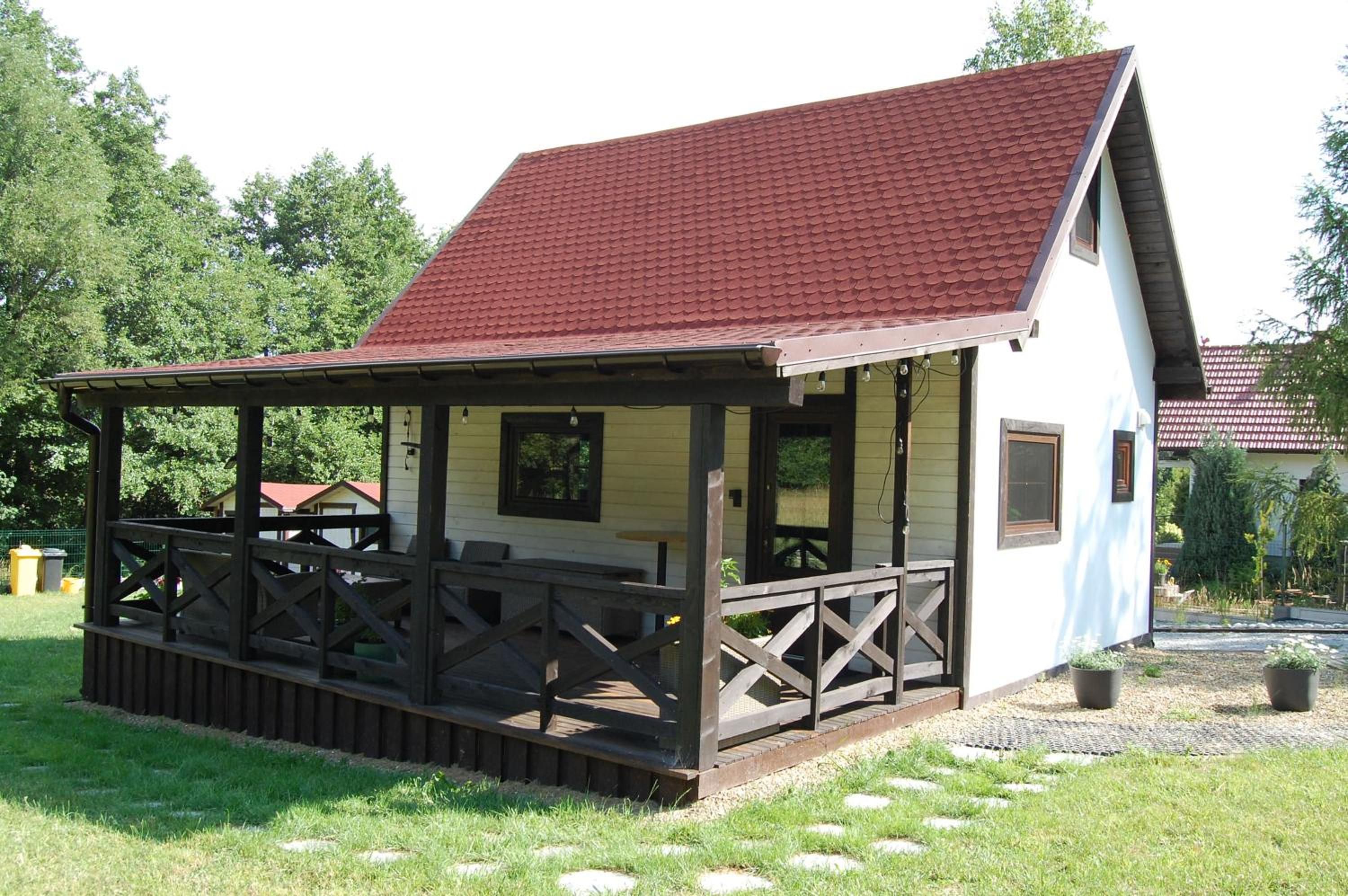 Biały domek z czerwonym dachem i zadaszonym drewnianym tarasem